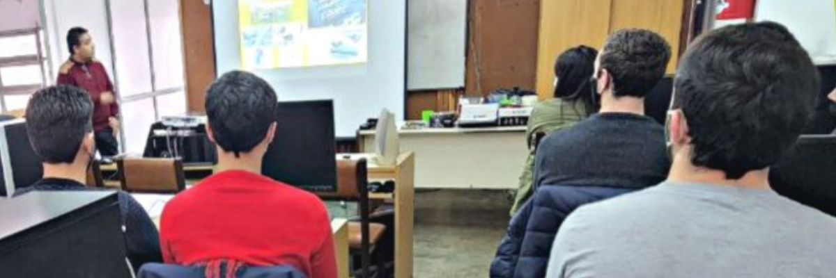 La información: Curso de Armado y Reparación PC se encuentra dispuesta en un rectágulo tipo llamada verde claro con letras blancas, de fondo una foto en un aula con computadoras, estudiantes y un profesor.